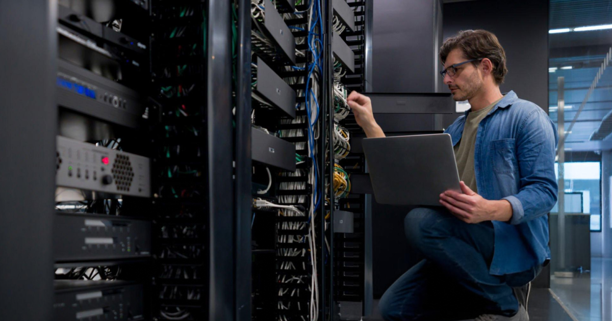 Technician with a laptop checking cabling in an open server rack